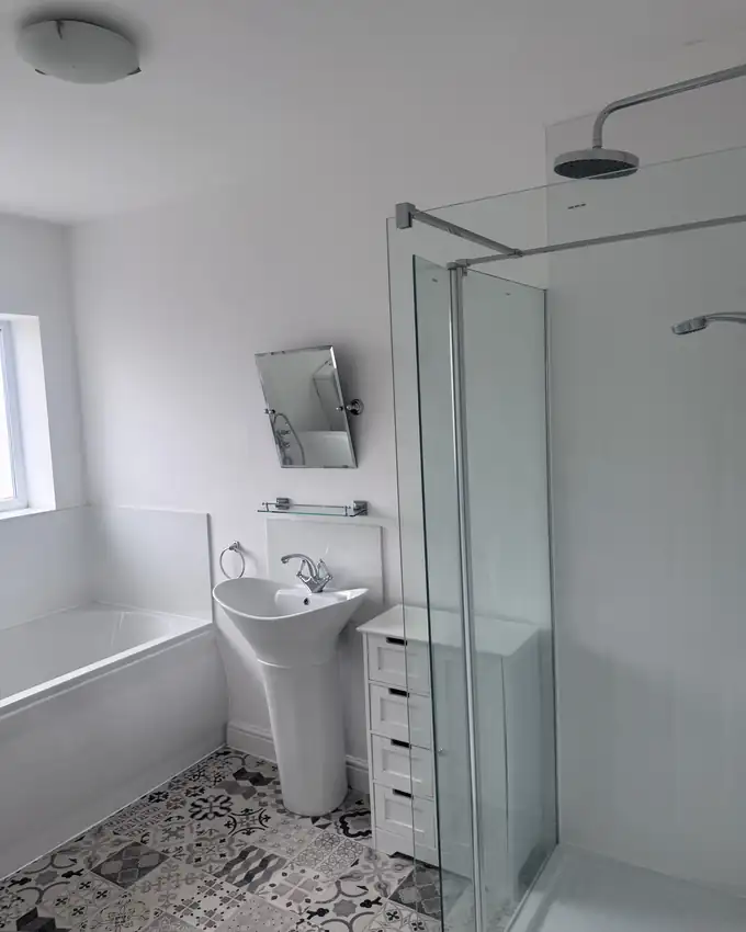 A spotless white bathroom with polished glass shower screen, basin and patterned tiled floor